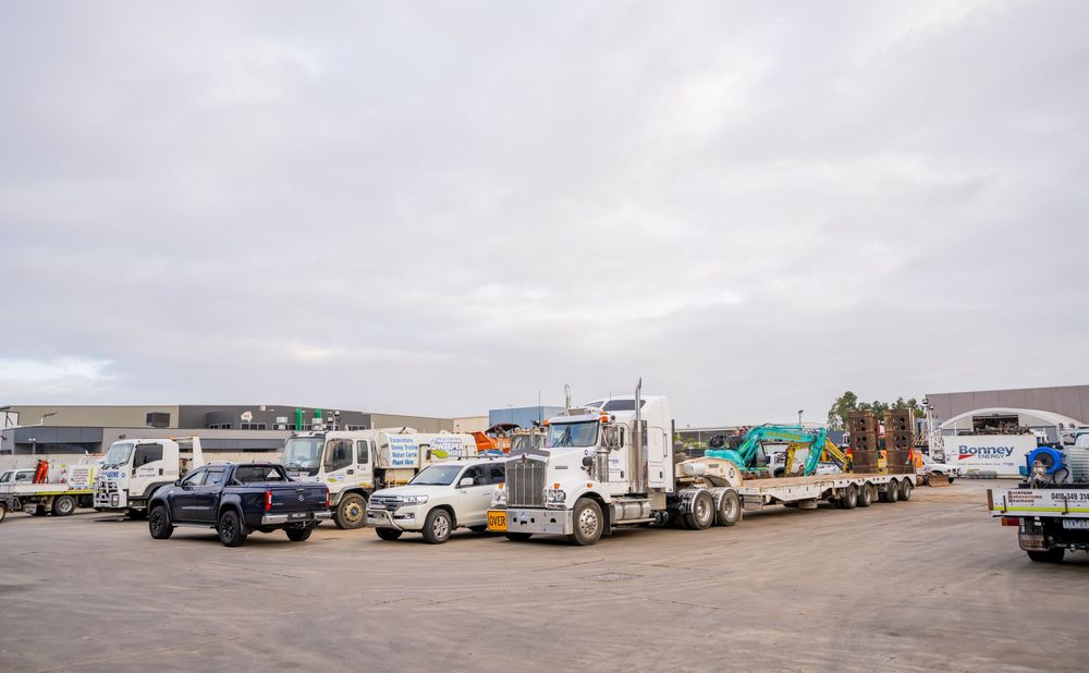 Multiple semi trucks and trailers parked in an industrial parking lot on a cloudy day.