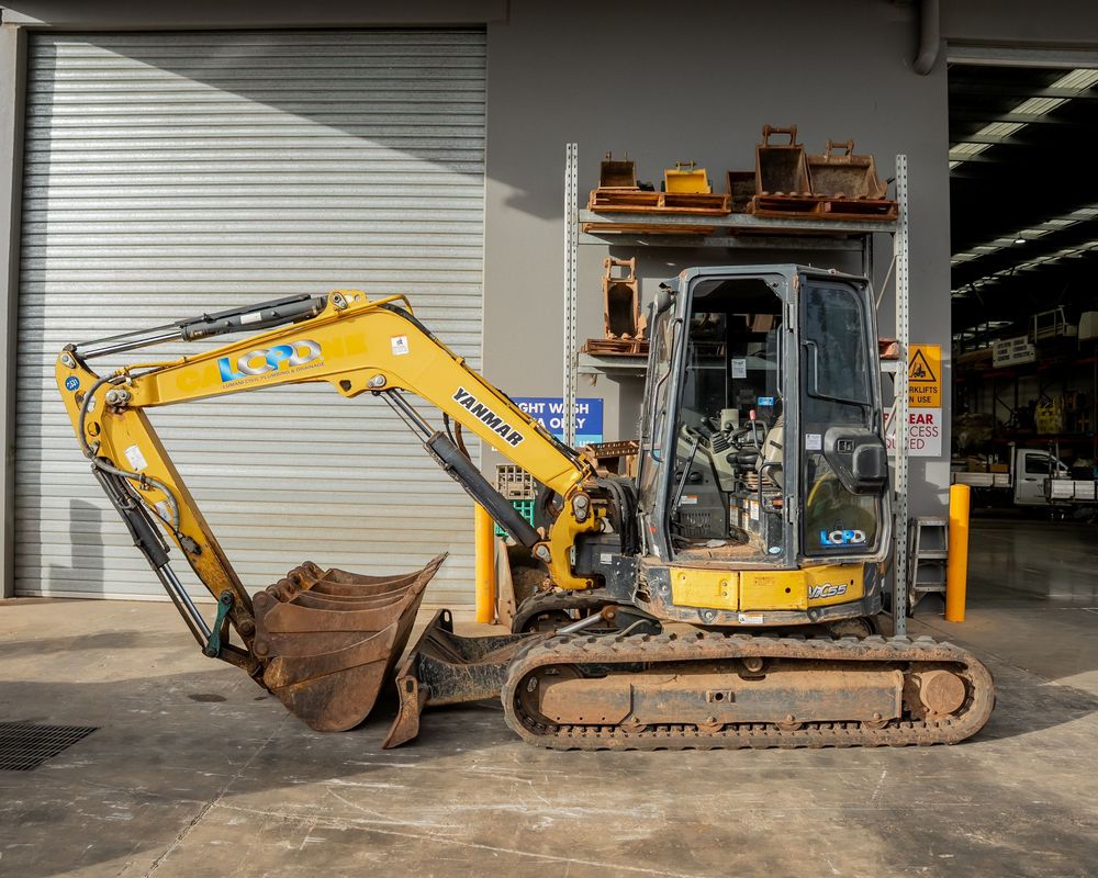 Yellow excavator machines parked in a row inside an industrial warehouse with concrete floors and white walls.