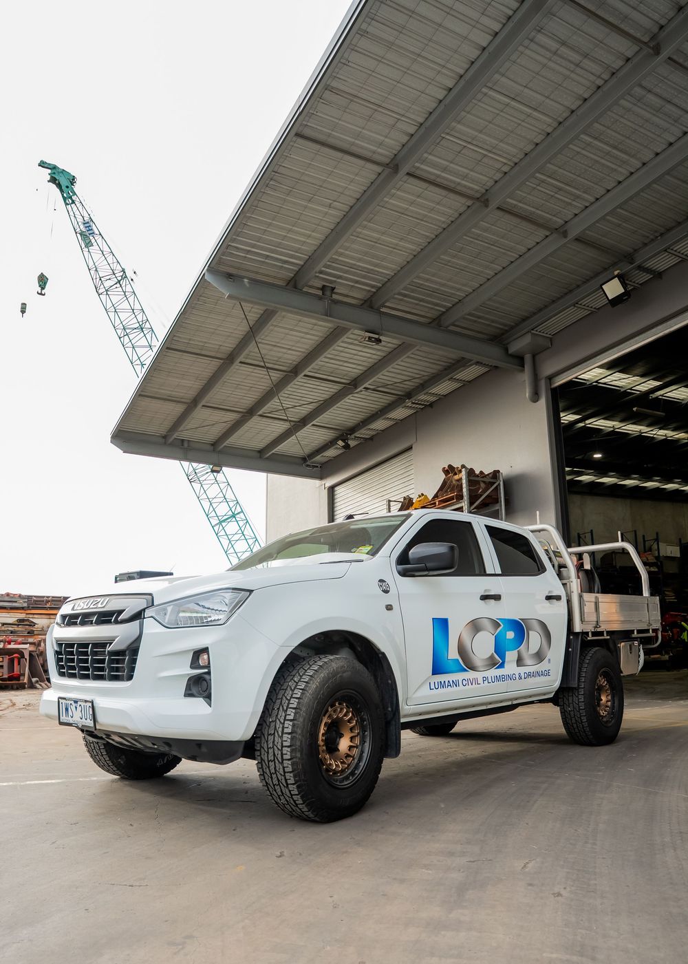 A white Isuzu D-Max pickup truck with LOOP branding parked under an industrial warehouse overhang with a crane visible.