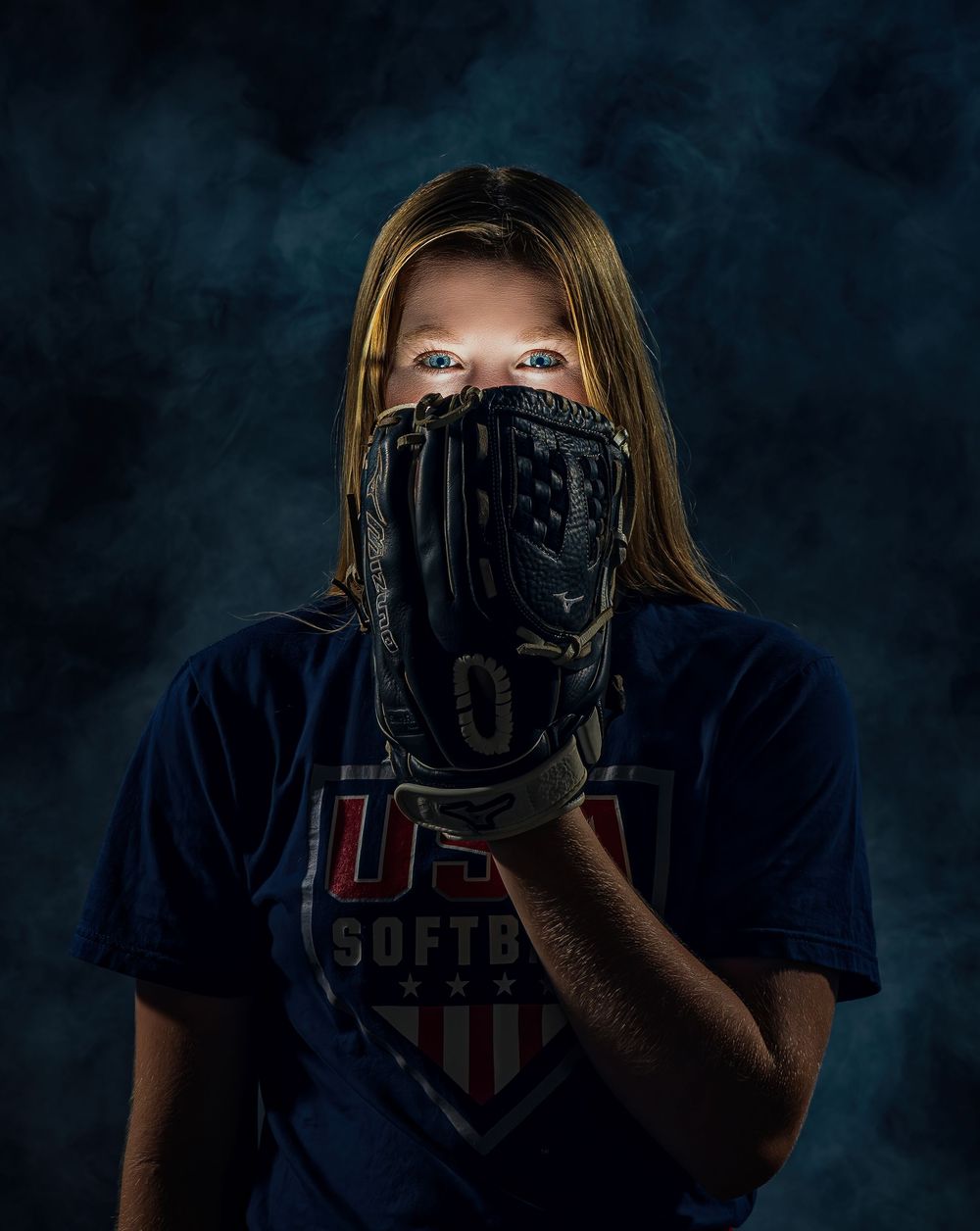 A photographer in a navy t-shirt holds up a camera to take photos against a dark studio background.