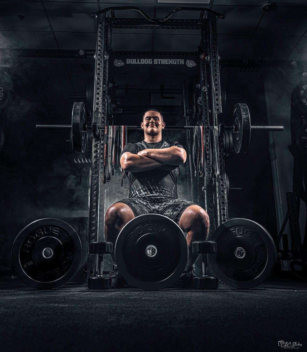A dramatic low-angle view of a powerlifter preparing to lift a heavy barbell in a dimly lit gym setting.