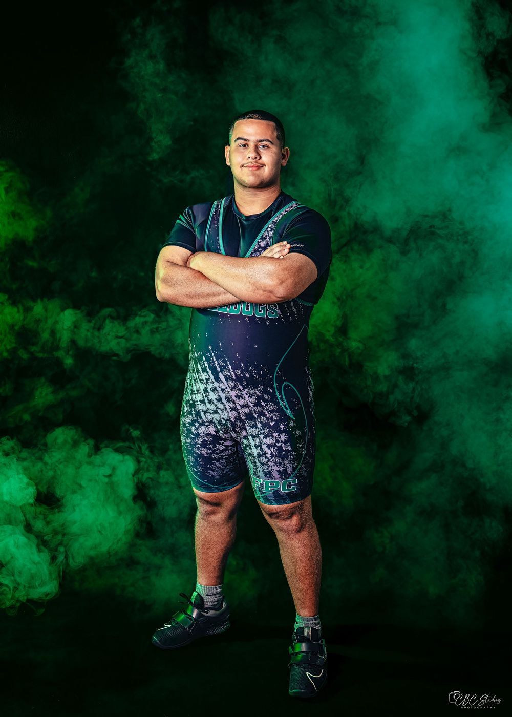 Athletic figure poses against dramatic green smoke background in stylish navy and teal patterned athletic wear.