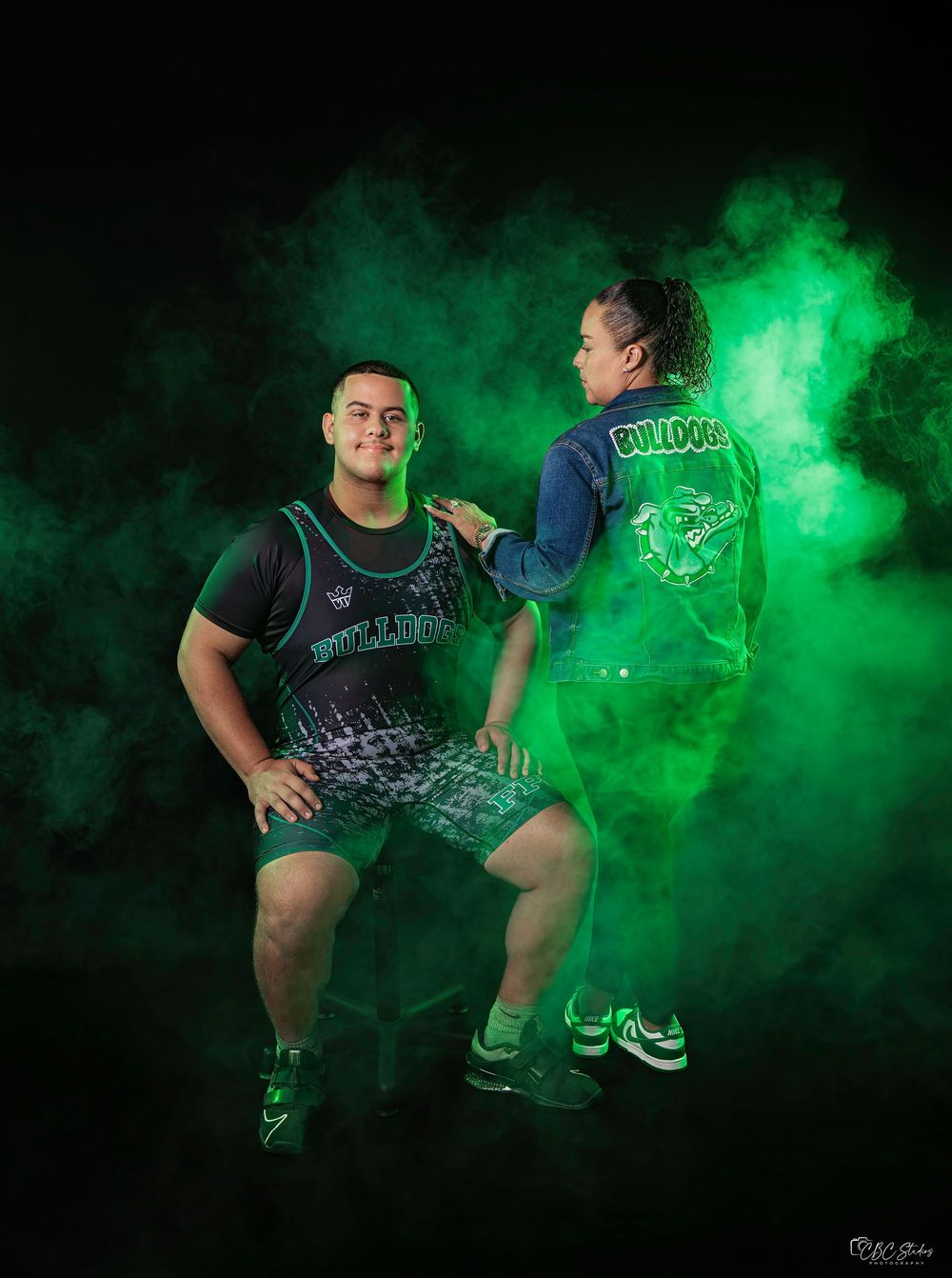 Athletic figures pose dramatically in green smoke for a stylized sports photo against black background.