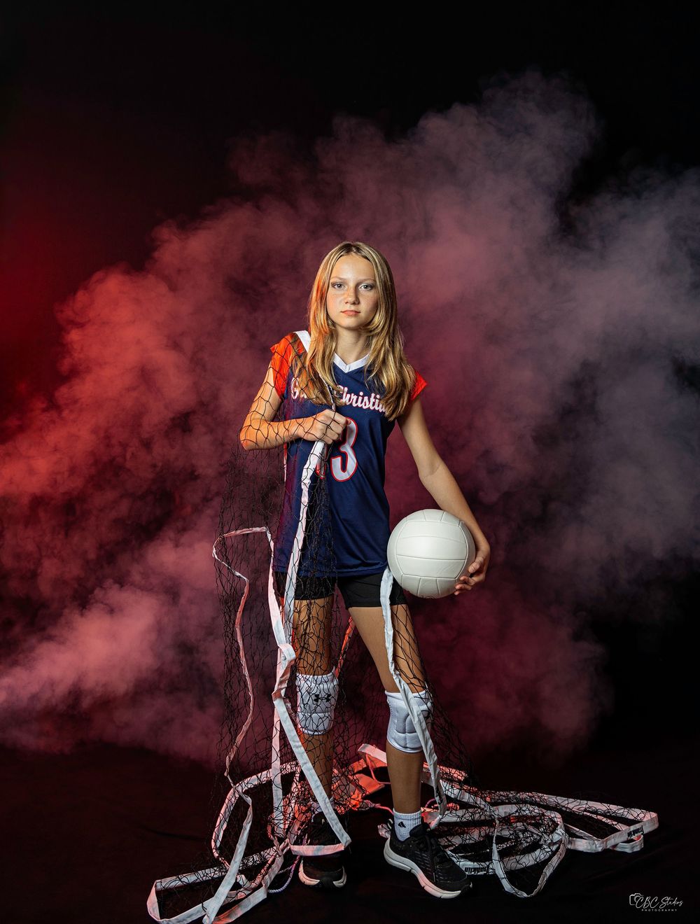 Volleyball player poses with ball and ropes against dramatic red smoke effect.