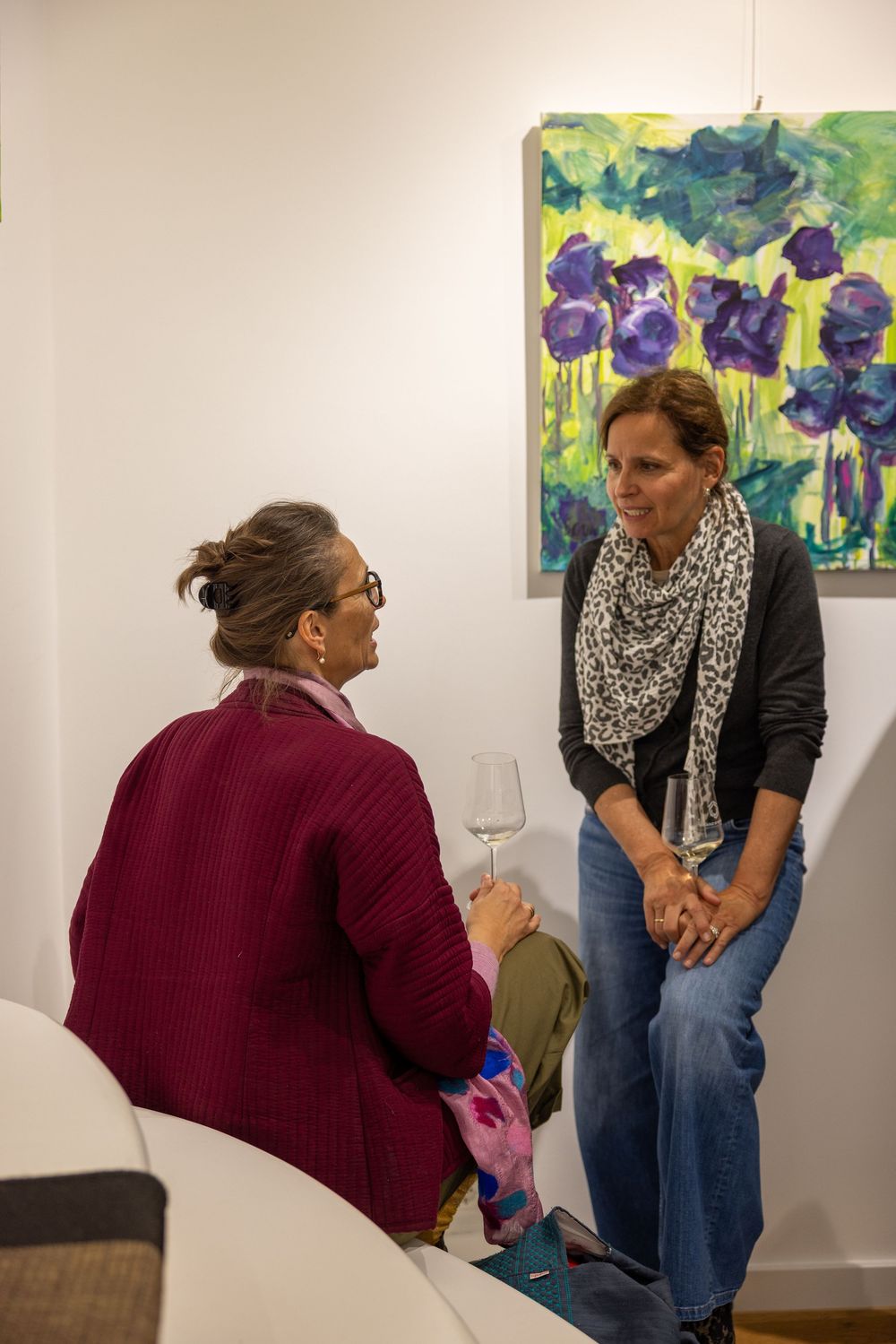 Gallery visitors examining colorful floral artwork in a white-walled exhibition space.