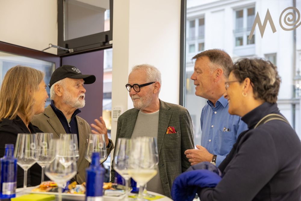 Gallery visitors engage in lively discussion during an art exhibition opening.