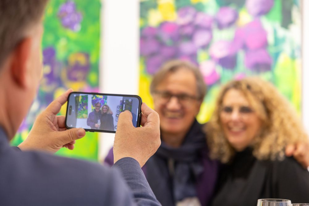 People gather at a gallery opening viewing vibrant floral-inspired artwork on white walls.