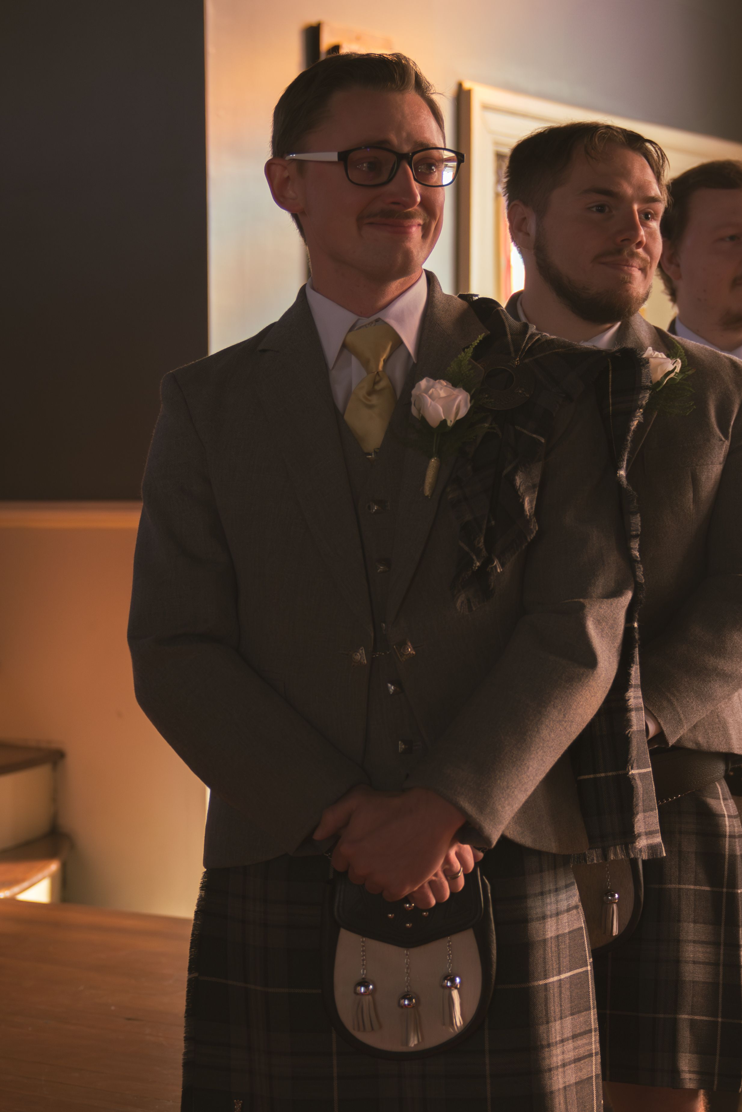 Groomsmen in gray suits and kilts standing together at a formal wedding event.