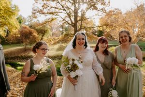 Wedding party in sage green dresses and formal attire poses outdoors during autumn.