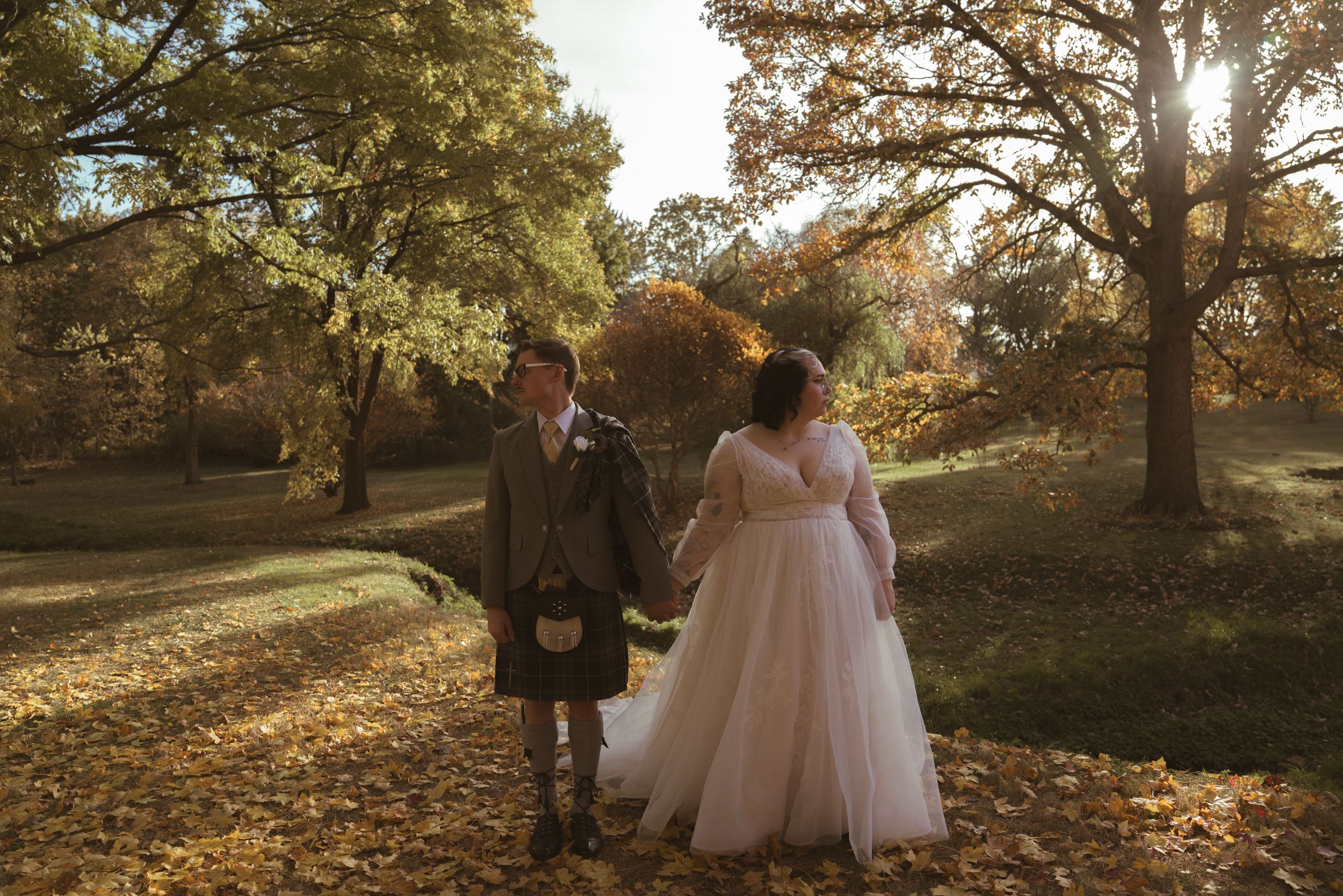Wedding party posing for photos in a sunlit autumn setting with golden leaves.