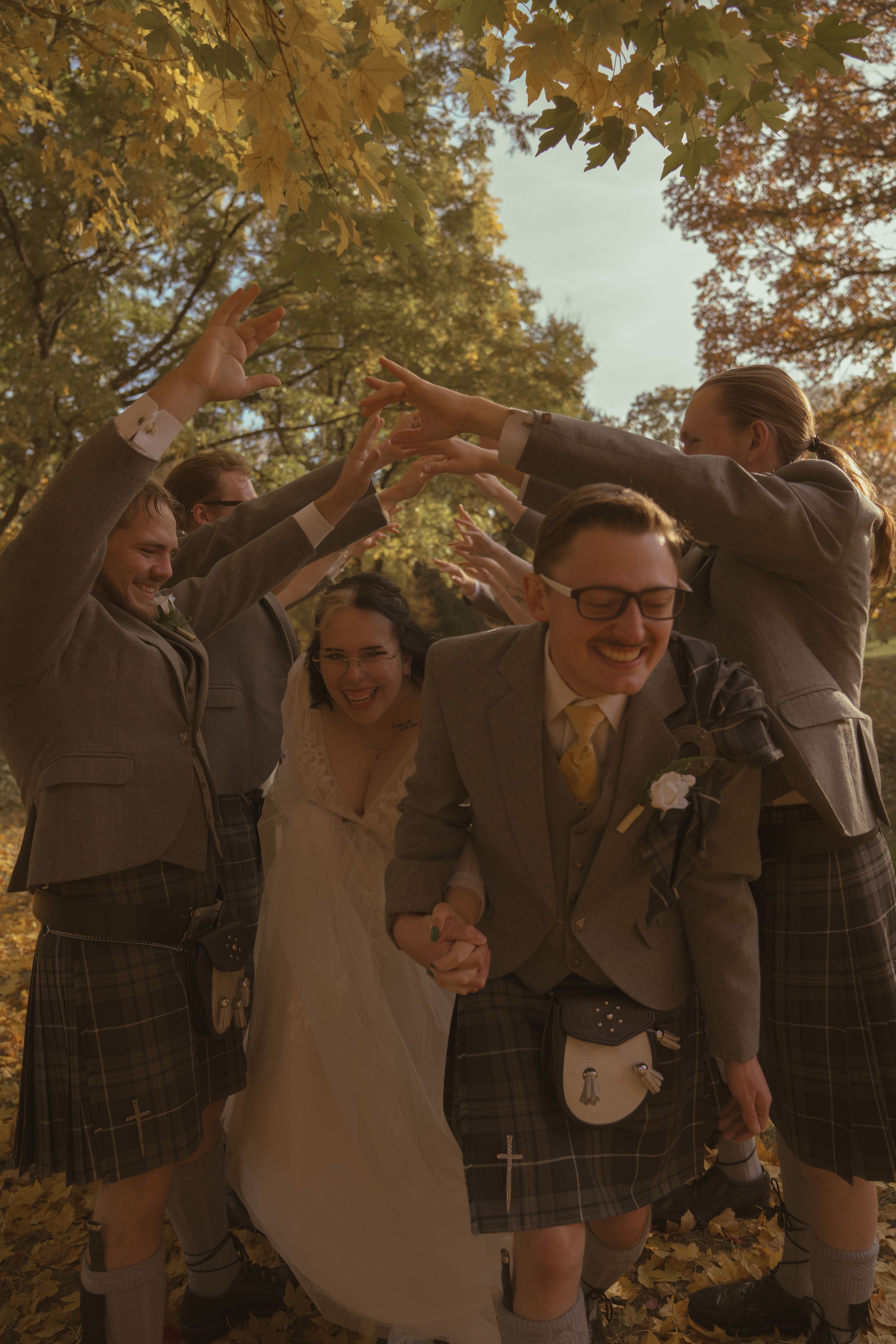 Wedding party having fun and posing playfully under autumn trees.