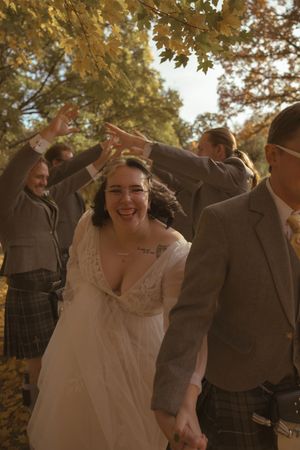 Wedding group celebrating with energetic poses in a scenic fall setting.