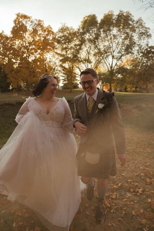 Newlyweds share a playful moment while walking through autumn leaves at sunset.