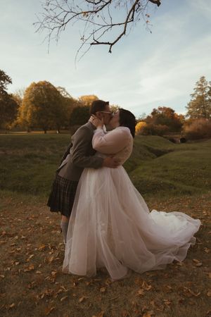 Romantic dip kiss between newlyweds surrounded by fallen autumn leaves.