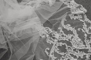Close-up detail of delicate white lace and tulle fabric from a bridal veil showing intricate floral patterns.