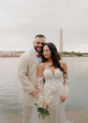 Wedding couple embraces near DC's Tidal Basin with Washington Monument visible in distance.