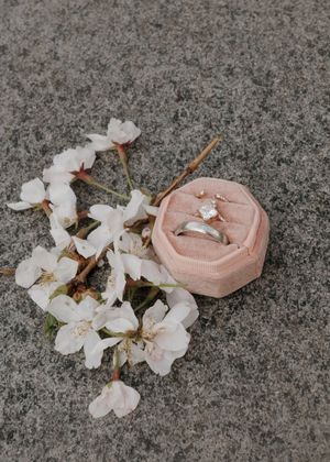 Wedding rings displayed in a pink velvet box with white cherry blossoms on stone surface.