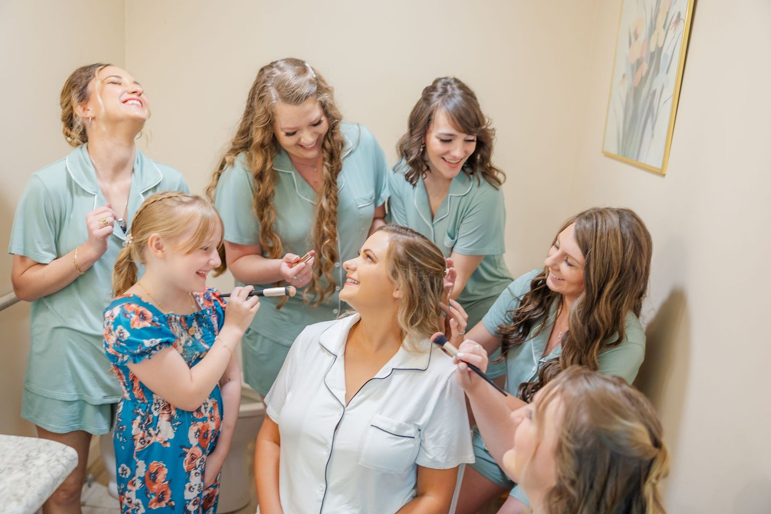A group of women in matching turquoise robes share joyful moments together while getting ready in a room.