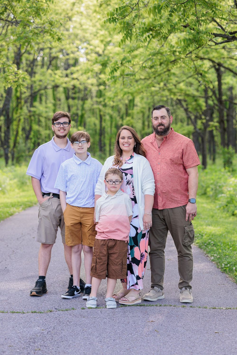 Family group portrait on a tree-lined path wearing coordinated casual outfits.