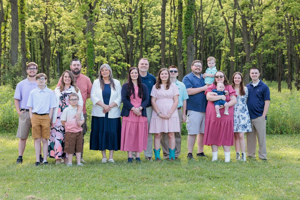 Large family group photo taken outdoors in a lush green wooded setting.