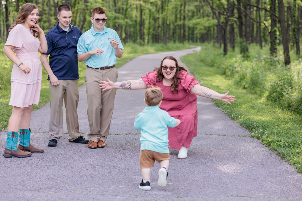 A candid family photo taken outdoors on a path surrounded by green trees and foliage.
