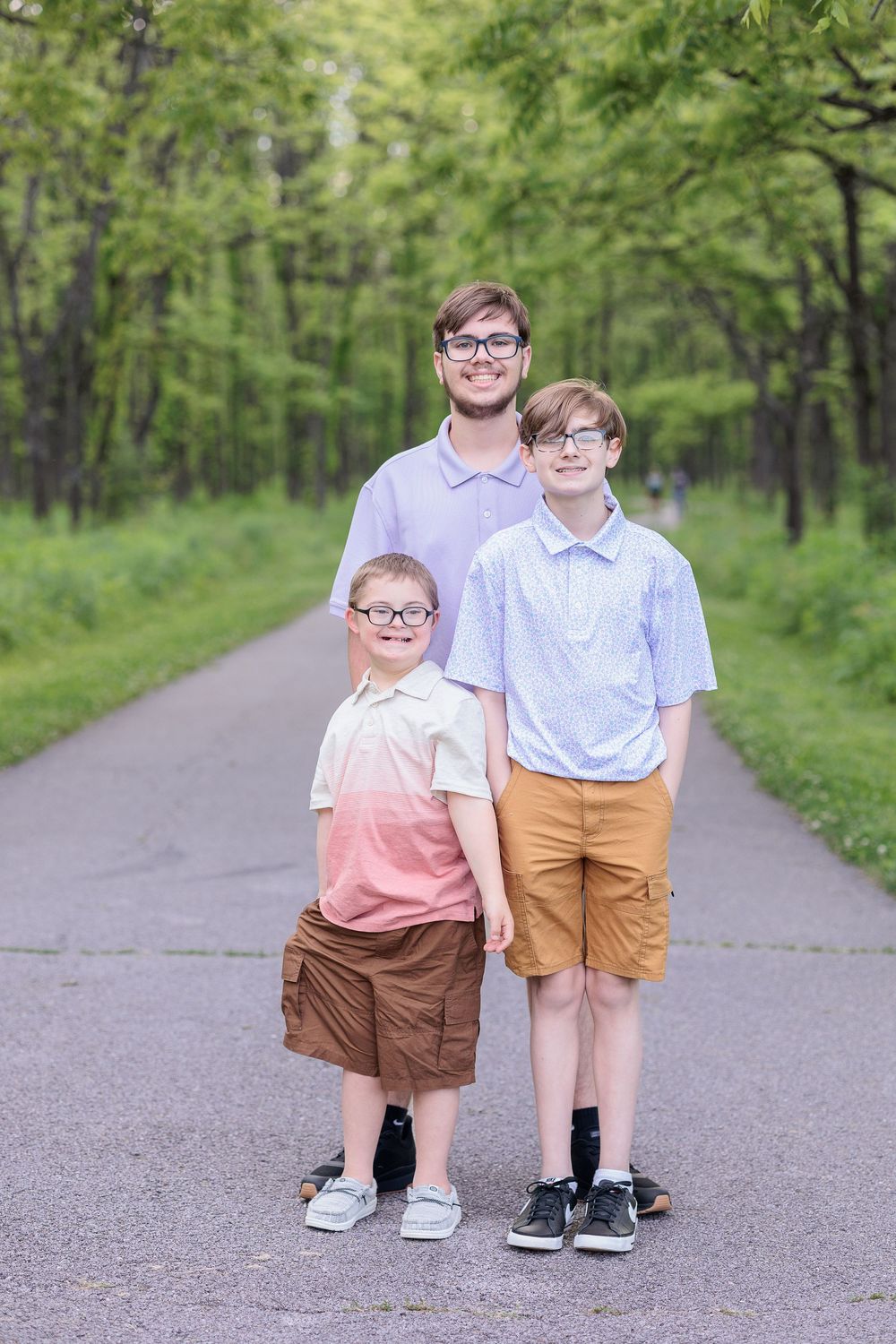 Three brothers standing together on a paved forest trail surrounded green trees.