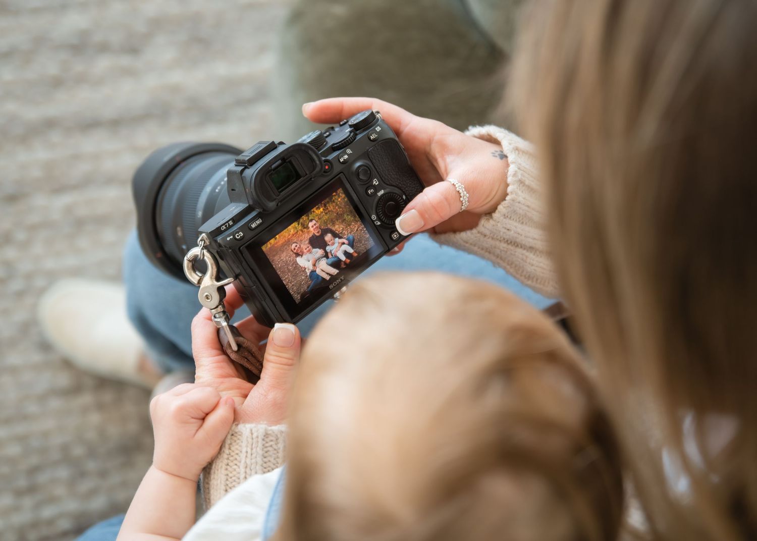 Person reviewing photos on digital camera display screen while holding camera with lens attached.