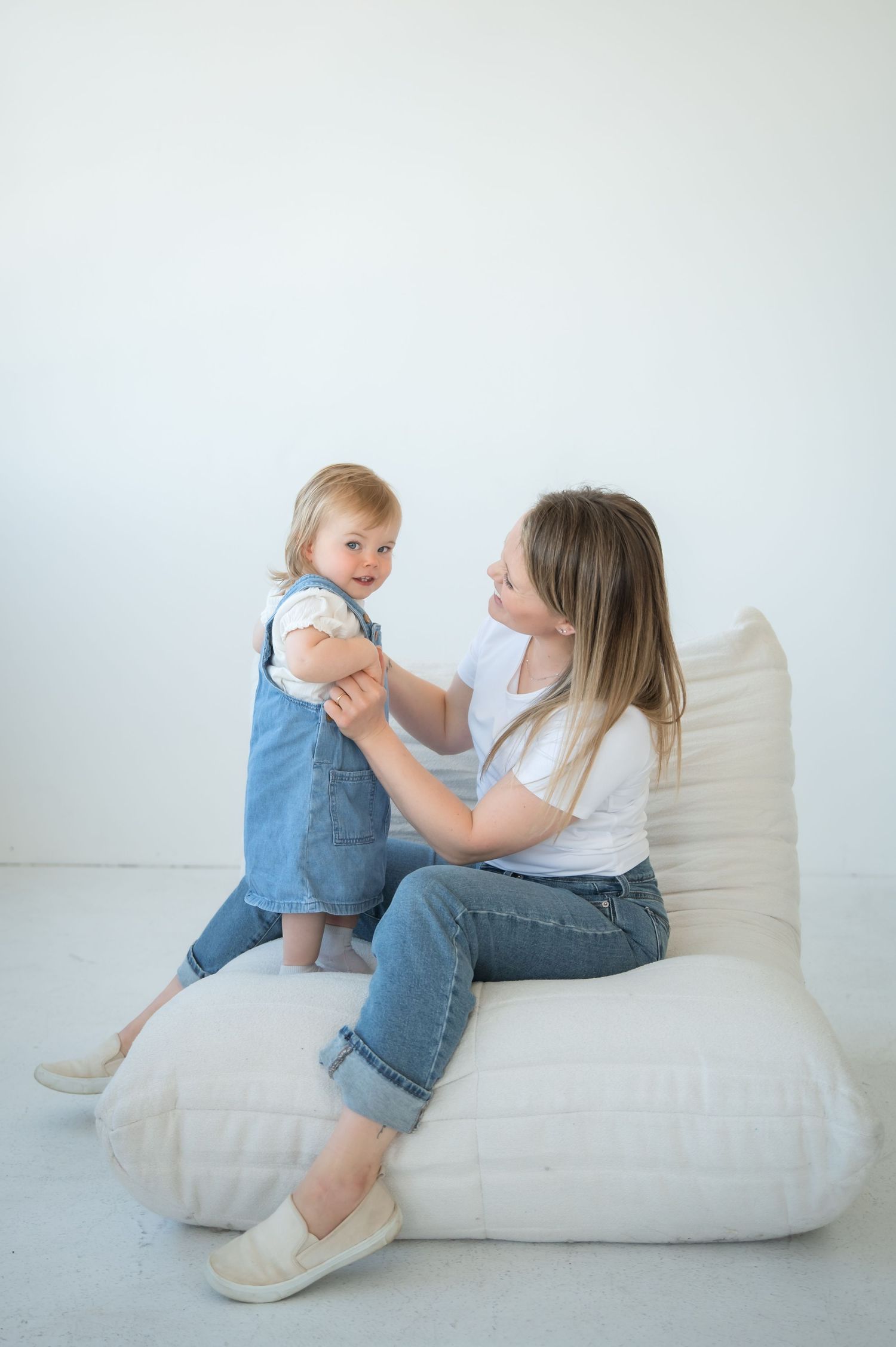 Parent and toddler in blue jeans and casual wear looking at something on the white floor in a four-panel progression.