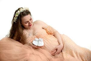 Artistic maternity photo showing an expectant mother in peach tones resting with small white baby shoes.
