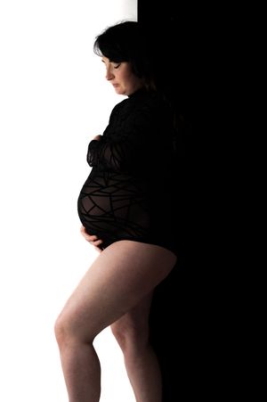 Dramatic silhouette maternity portrait with black and white contrast showing elegant profile pose.