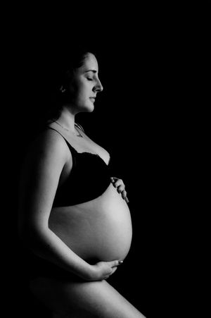 Black and white artistic maternity photo showing an expectant mother in profile against a dark background.