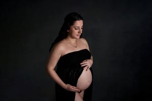 Maternity portrait featuring strapless black velvet gown against dark background with soft lighting.