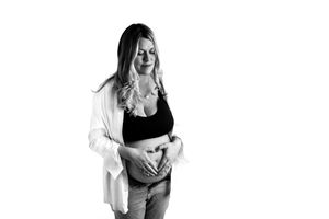 A person wearing a white cardigan and black top holds their pregnant belly while standing against a white backdrop.