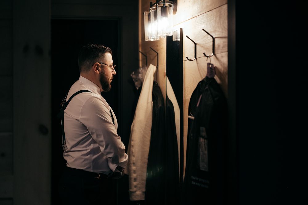 A person in a dress shirt hangs up clothing in a dimly lit closet or wardrobe area.