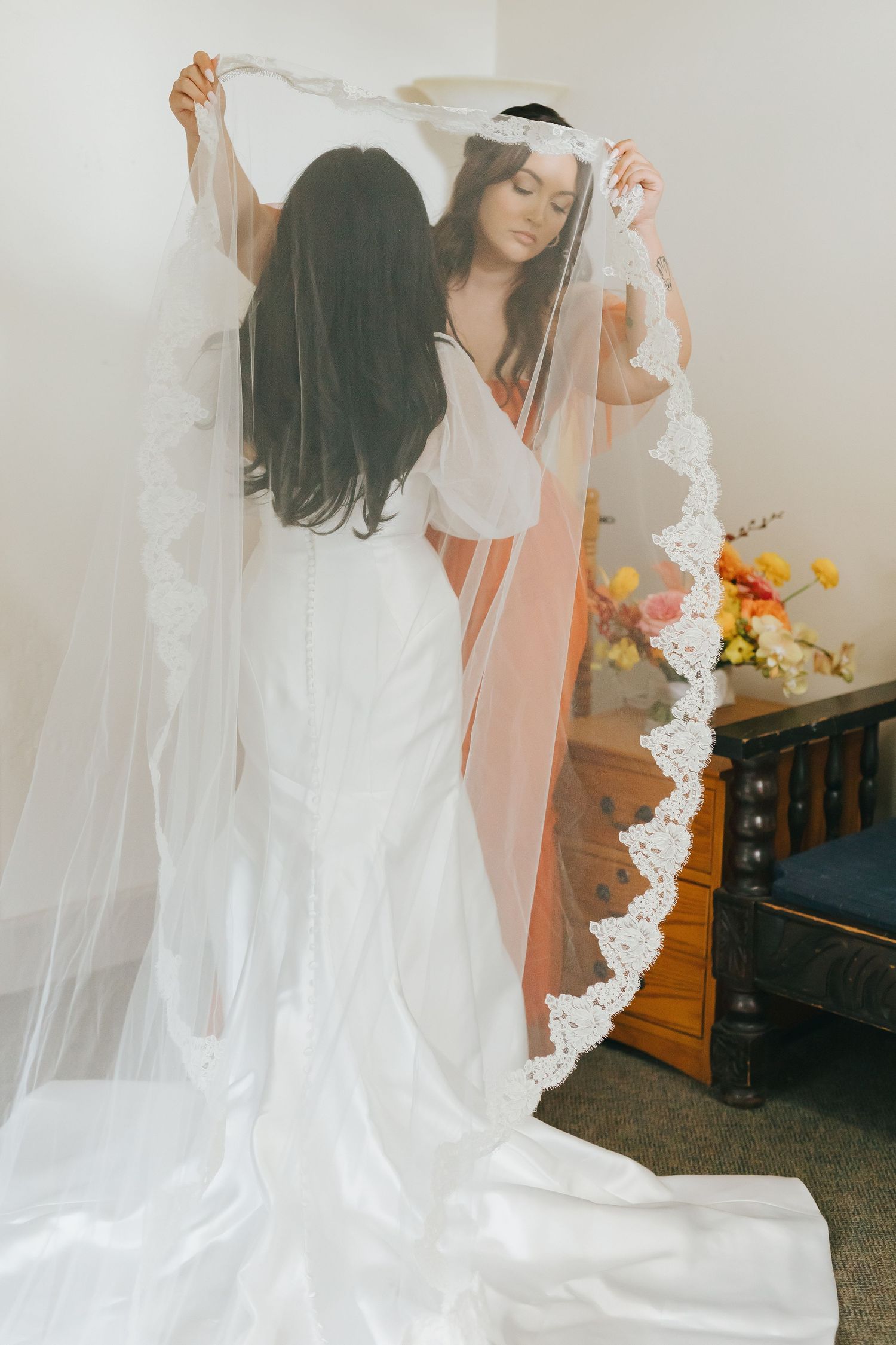 A wedding dress fitting session showing a long white gown with delicate lace veil in natural light.