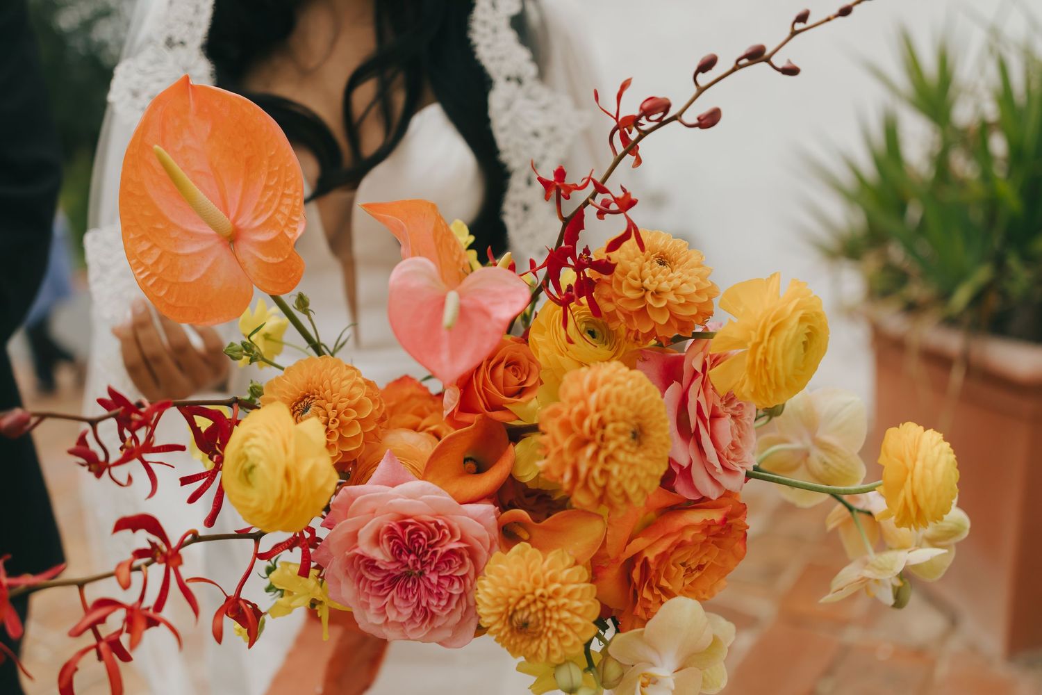 Vibrant floral arrangement featuring orange anthurium, yellow ranunculus, and red orchid branches in warm autumn tones.