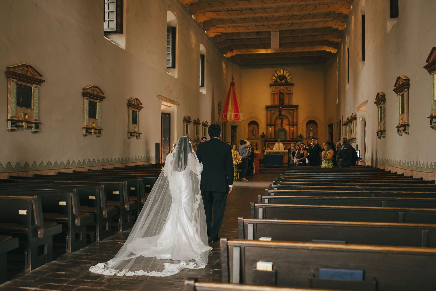 Interior view of a Catholic church sanctuary with wooden pews and vaulted ceiling lit by warm natural light.