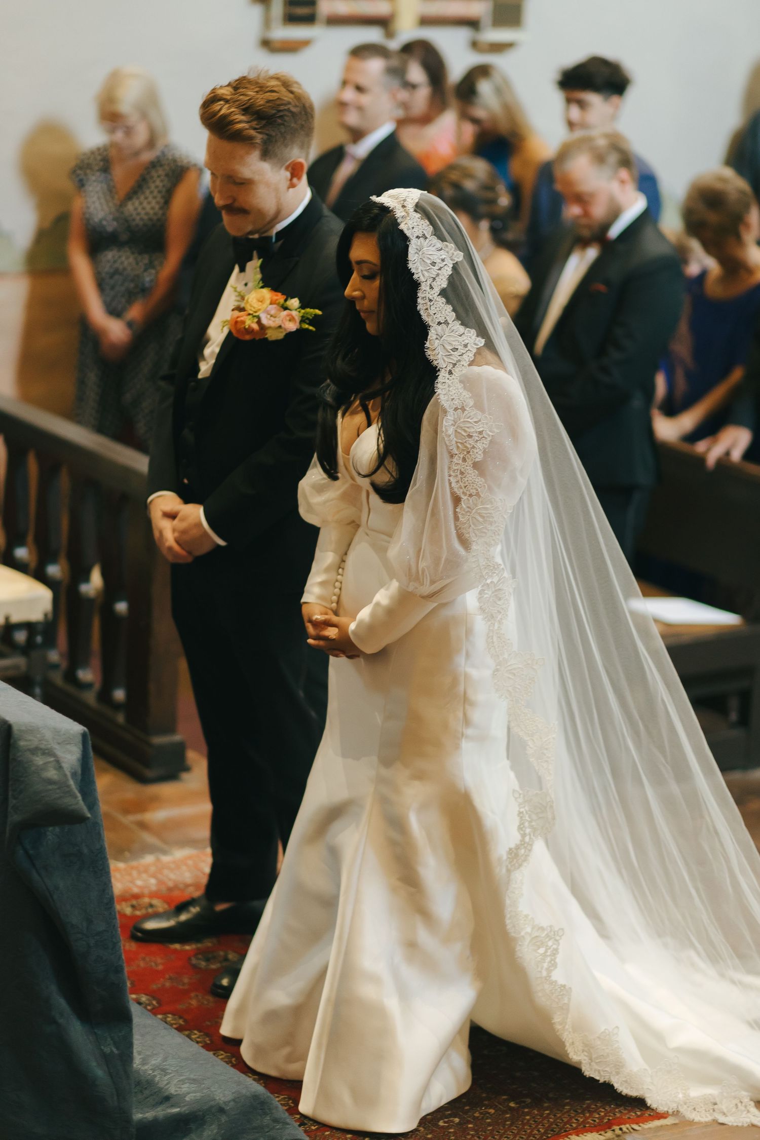 A couple shares an intimate moment during their wedding ceremony in a church while guests look on.