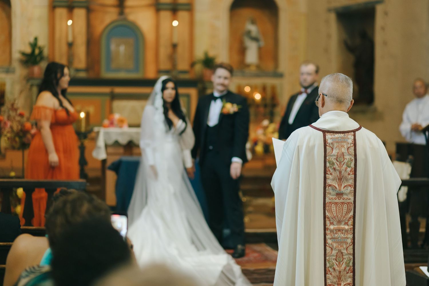 Catholic wedding ceremony in progress with priest in ornate vestments officiating in traditional church interior.