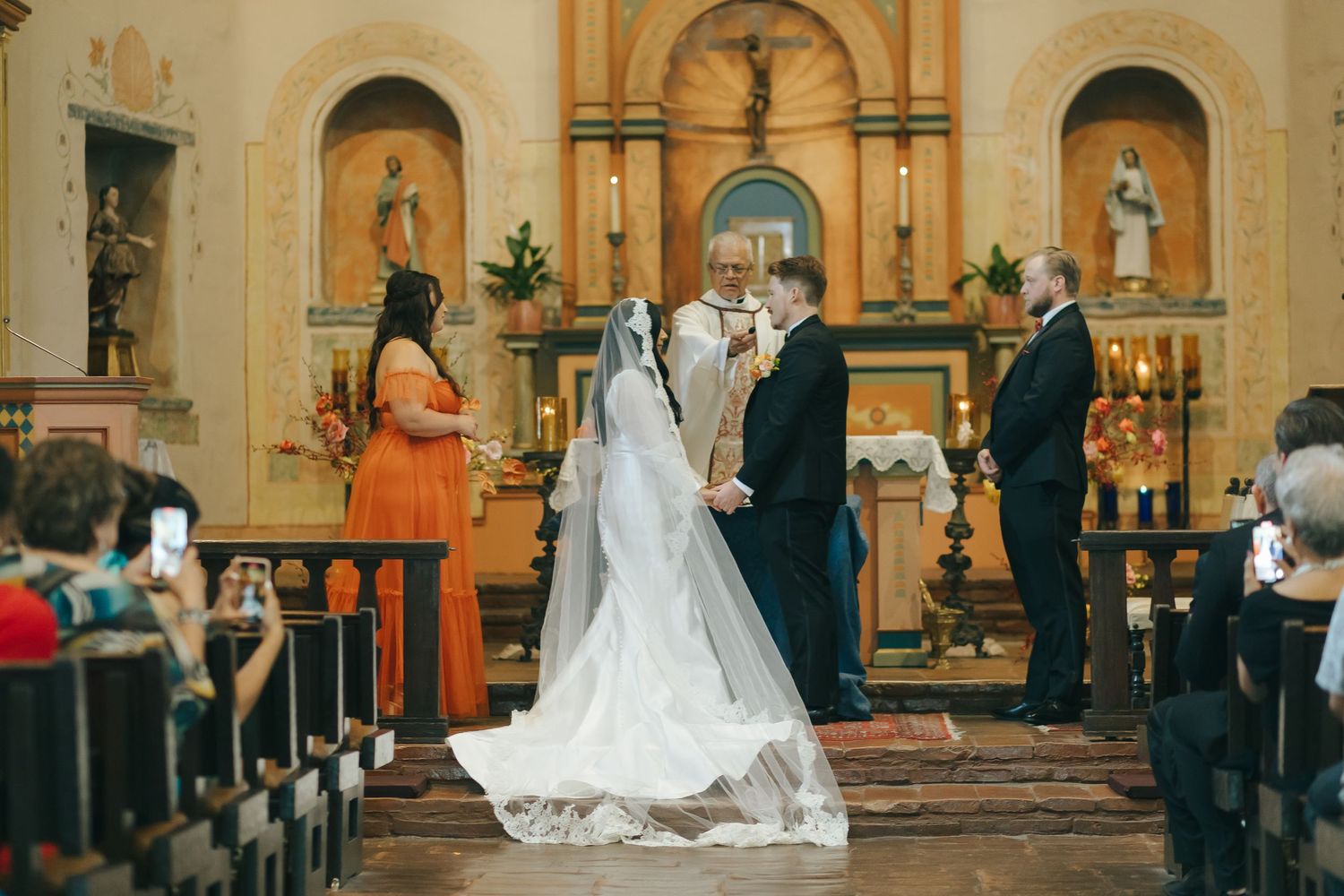 Wedding ceremony taking place inside historic Catholic church with decorative altar and wooden pews.