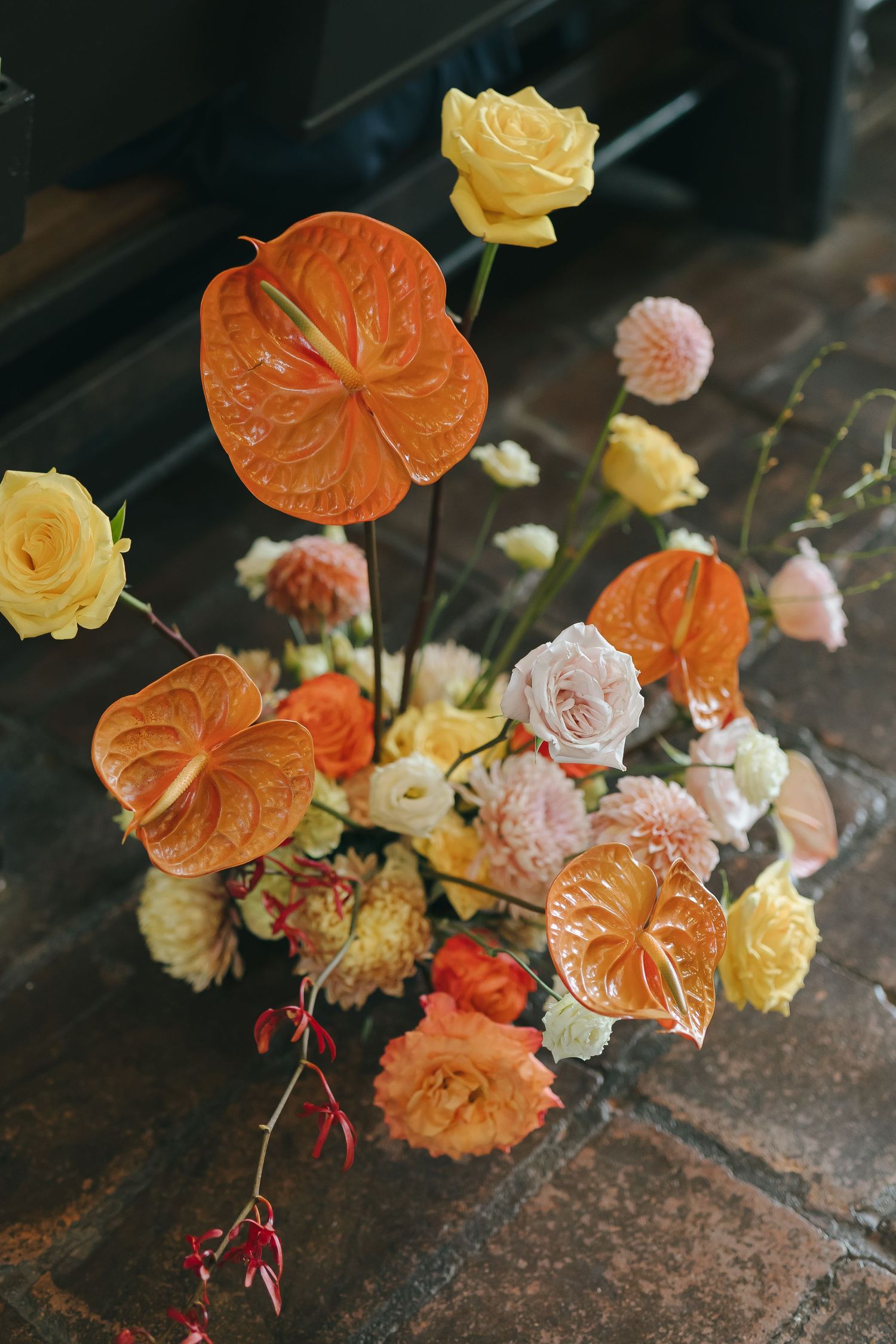 Stunning floral arrangement with orange anthuriums, yellow roses, and pink blooms on a rustic surface.