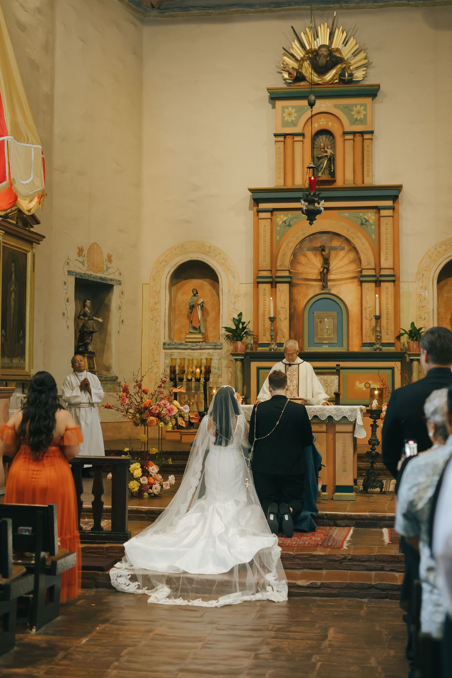 A bride and groom stand before an ornate altar during their Catholic church wedding ceremony.