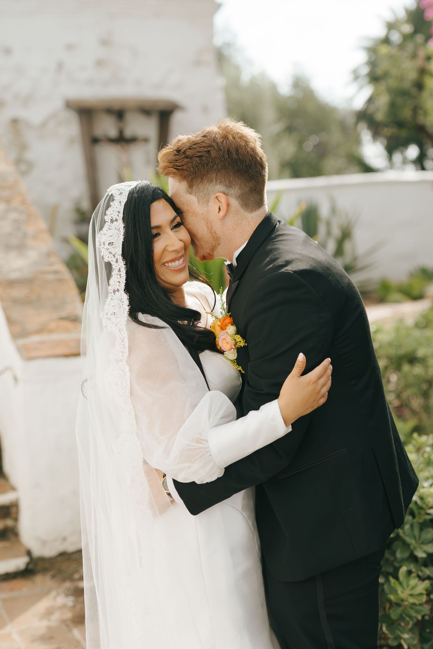 Joyful wedding moment captured in outdoor garden setting with white lace veil and flowers.