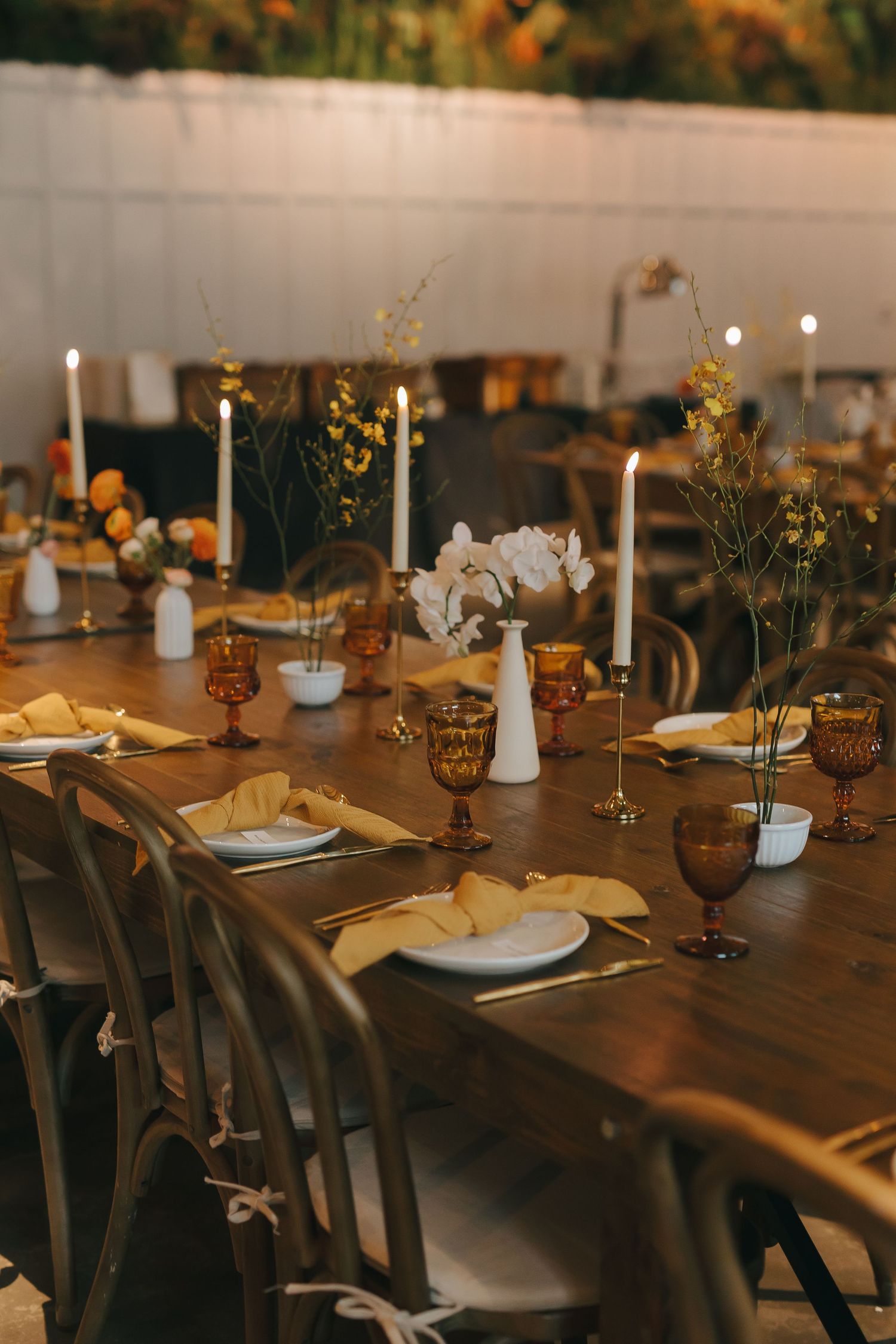 Elegant wedding reception table with amber glassware, white candles, and delicate floral arrangements.