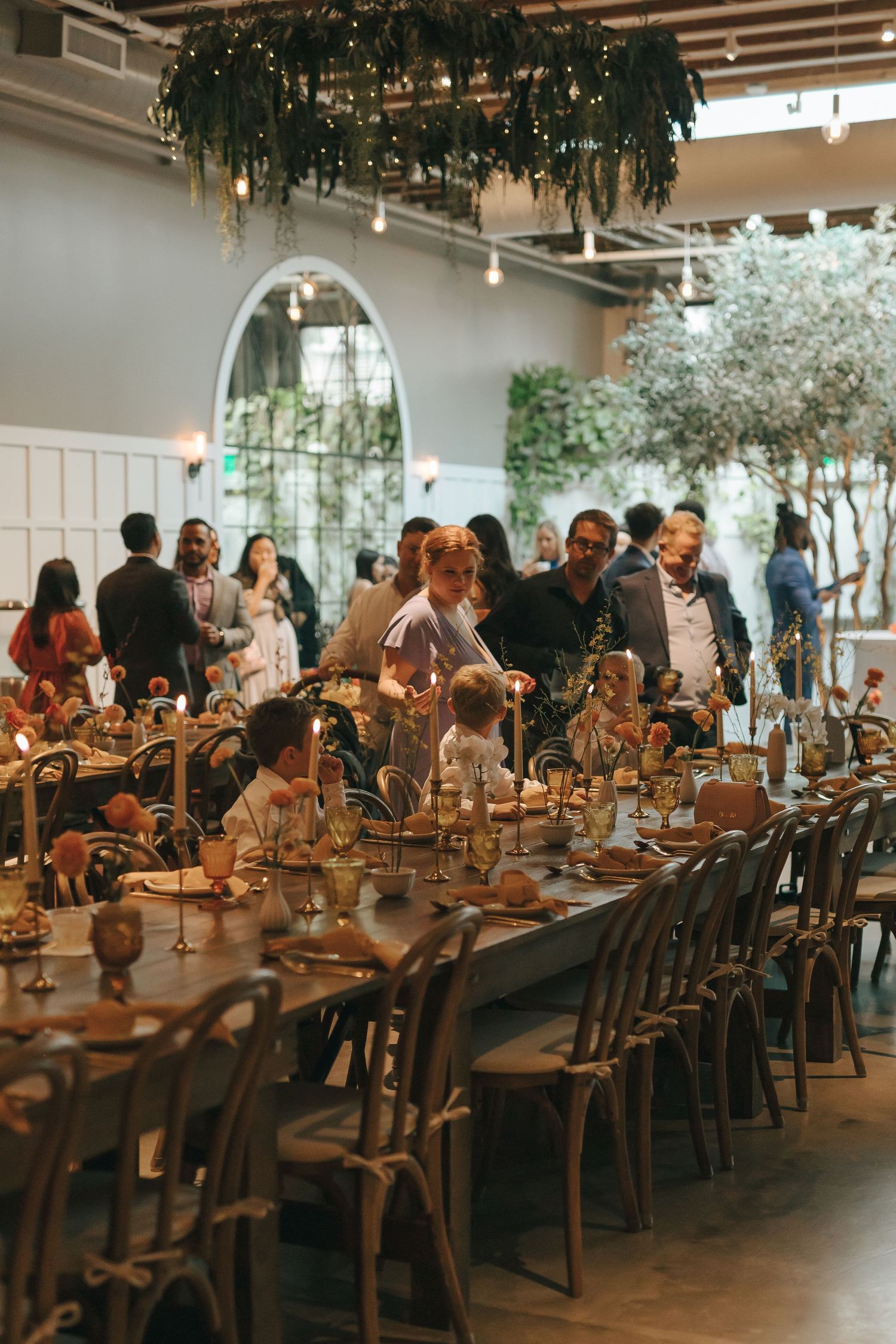 Wedding reception venue with long tables and hanging greenery creating an intimate dining atmosphere.