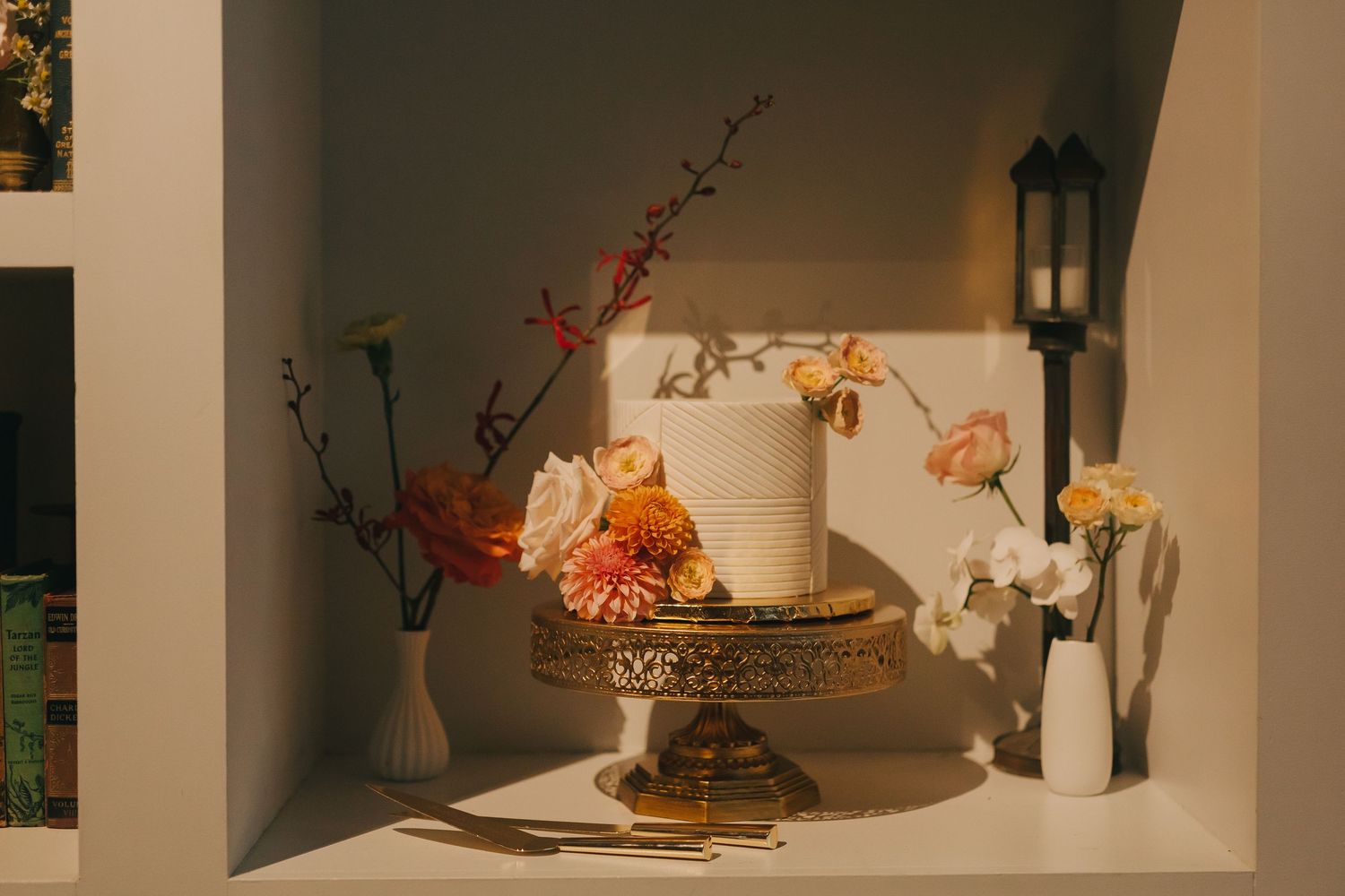 White tiered wedding cake decorated with orange and yellow flowers on an ornate gold stand.