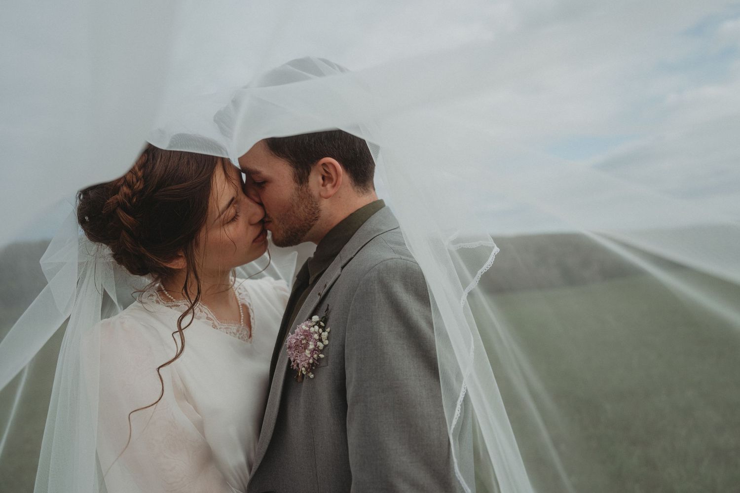 Intimate wedding portrait with flowing veil against misty mountain backdrop.
