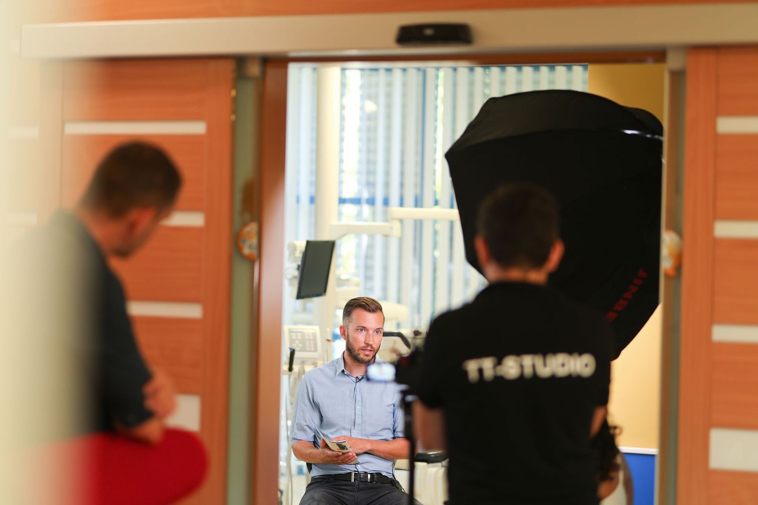 Two people work on lighting equipment in a TV studio with orange walls.