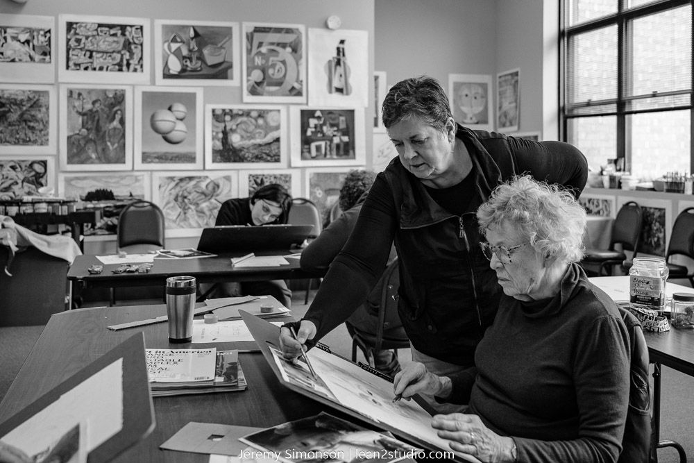 Two people working together at a desk in an art studio with illustrated artwork displayed on the walls in black and white.
