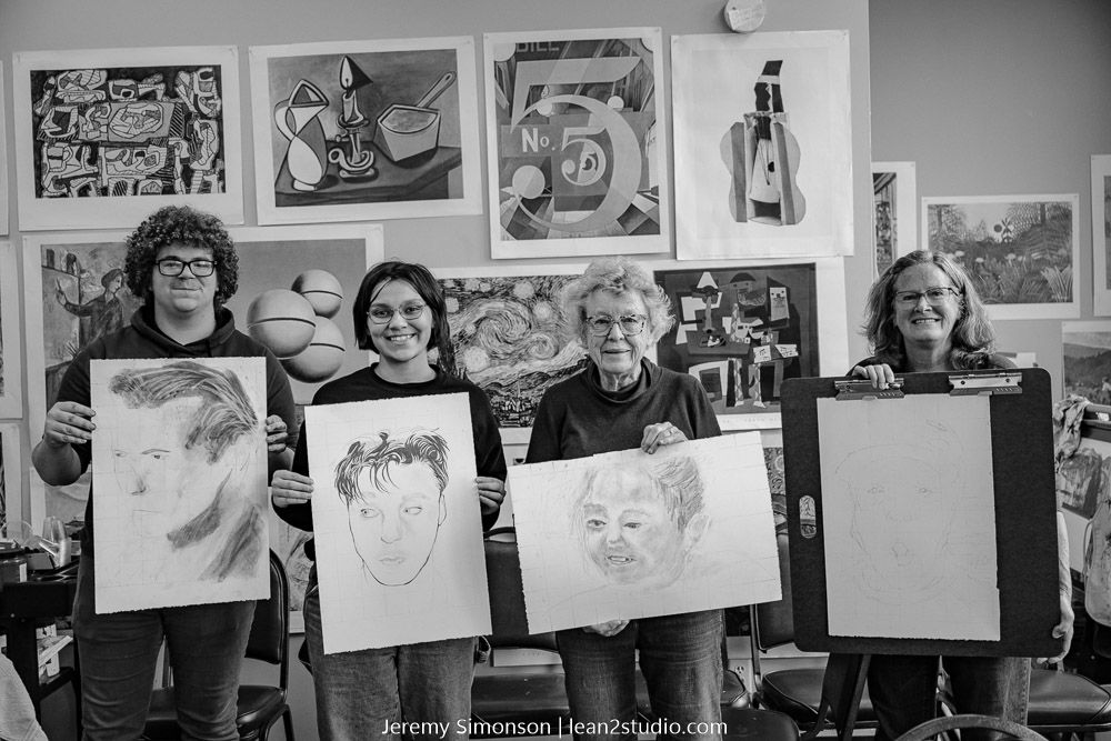 A black and white photograph shows art students displaying their drawings during a class session at an art studio.